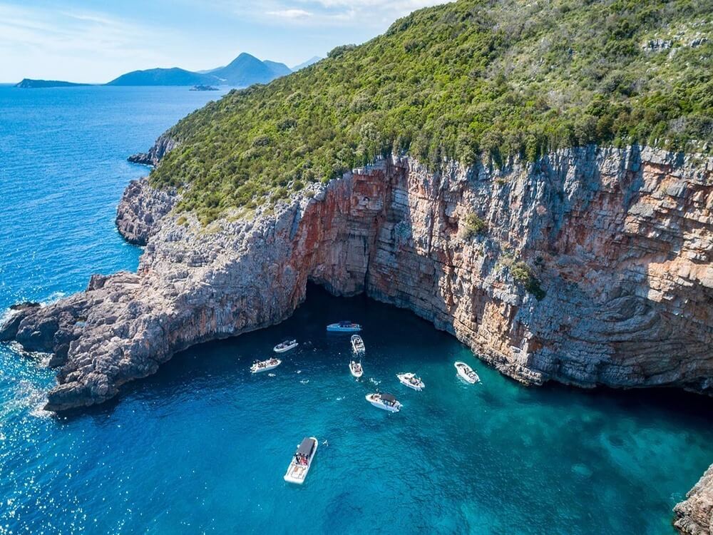 Aerial view of the turquoise Blue Cave on the Lustica Peninsula with several small boats anchored inside, Montenegro