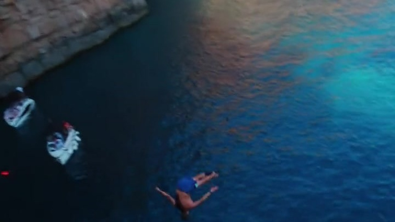 A diver mid-jump from a Blue Cave ledge, two of our boats holding position in the water below during the Orlando Duque exhibition